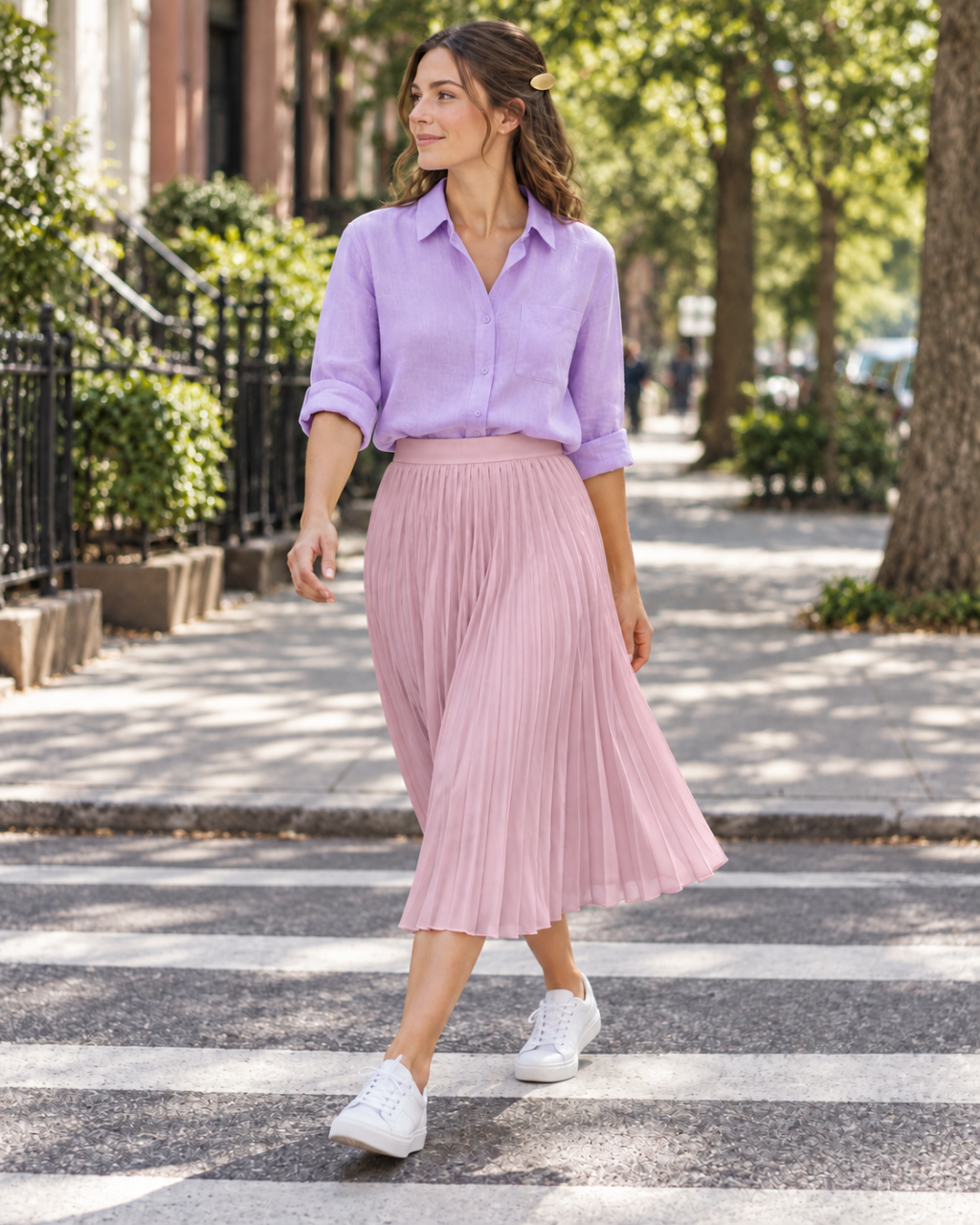 An adult woman wearing a lavender shirt, rose-pink pleated midi skirt, white sneakers and a small gold barrette.